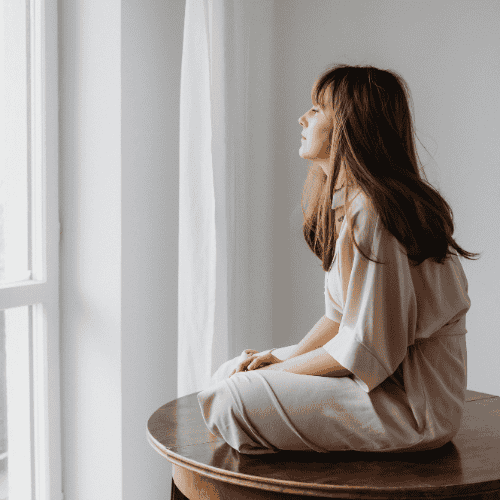 Frau im Alltag die nachdenklich aus dem Fenster sieht.